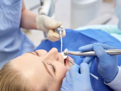 woman lying in dental chair with dentists looking at her mouth