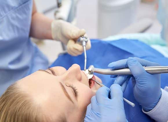woman lying in dental chair with dentists looking at her mouth