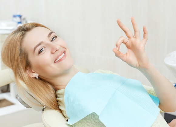 woman lying in dental chair givng an "OK" symbol with her fingers