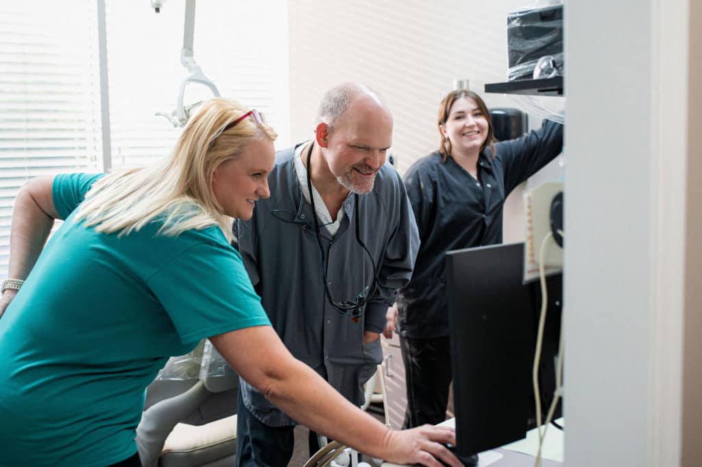 ChatGPT A dental team reviewing patient information on a computer screen, with one team member pointing at the monitor while the others look on and smile.