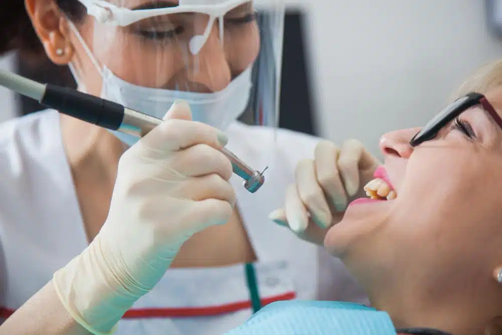 woman with glasses receiving treatment from dentists with mask and clear face covering