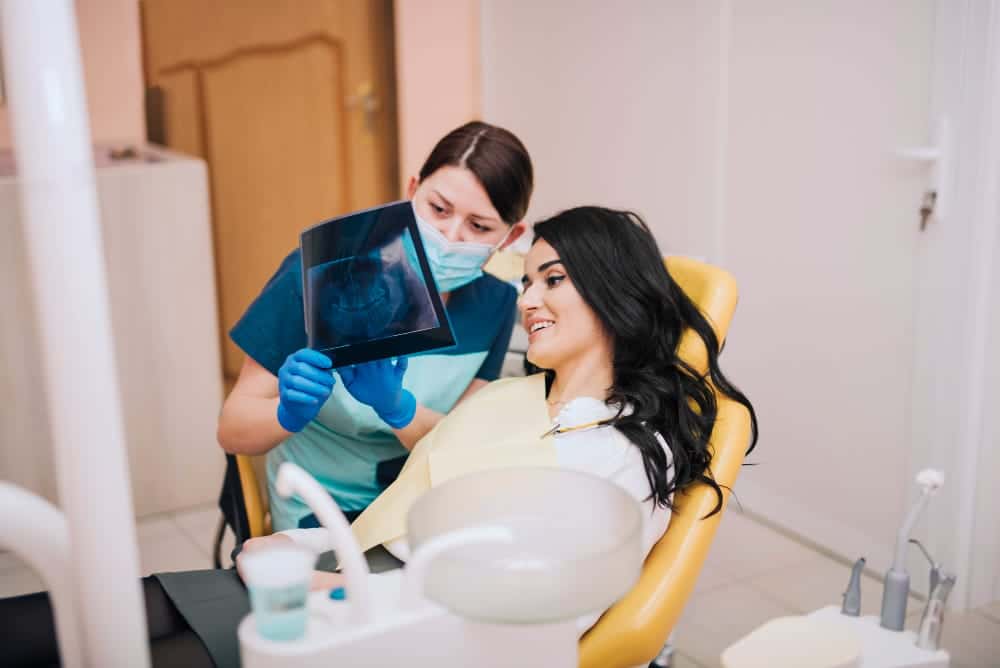 Dentist and patient reviewing a dental X-ray for preventive care. Dentist pointing at X-ray on computer screen, explaining details to attentive patient. Collaborative approach to oral health.